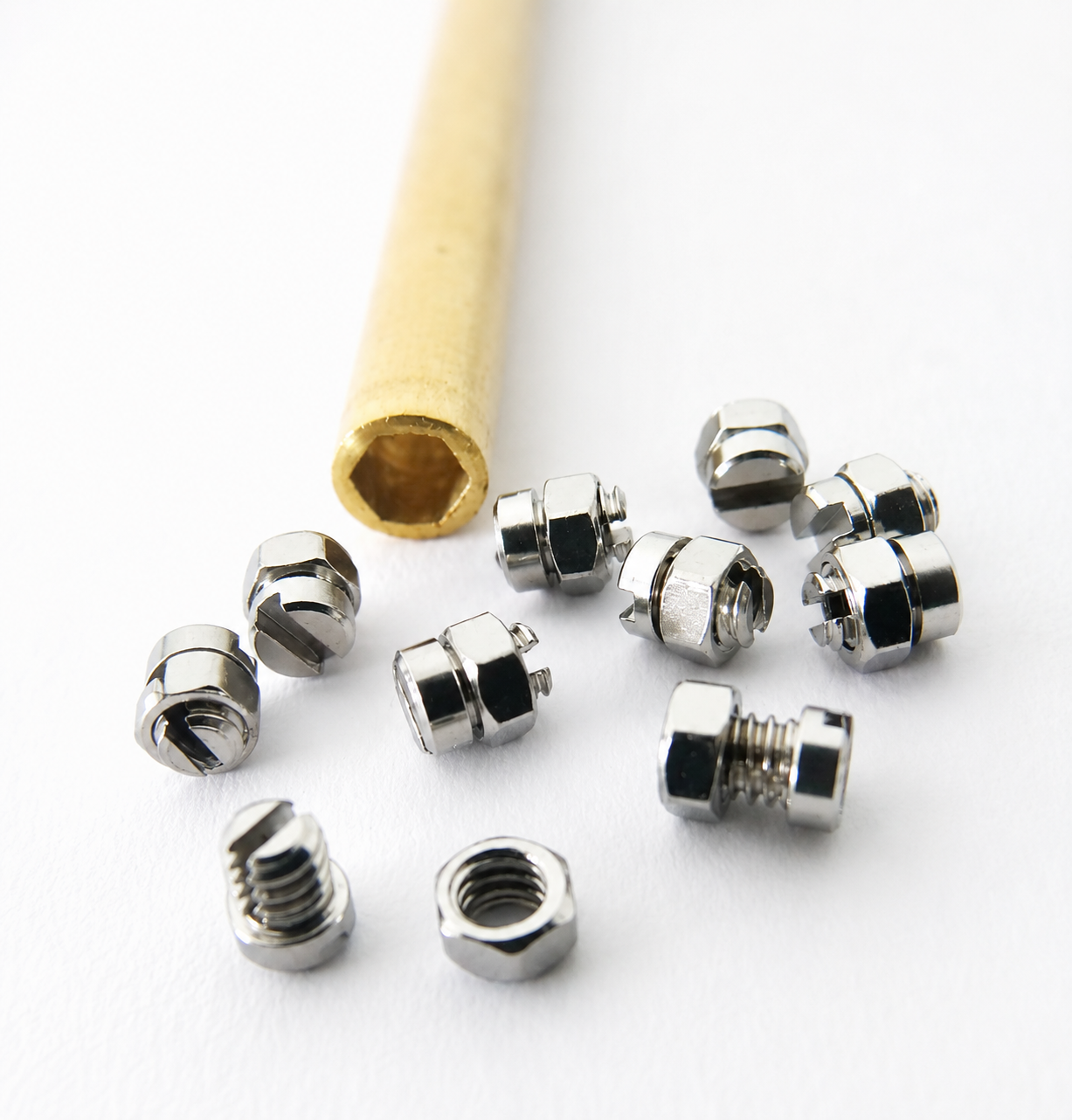 Metal hex nuts scattered on a white surface with a wooden hex key.