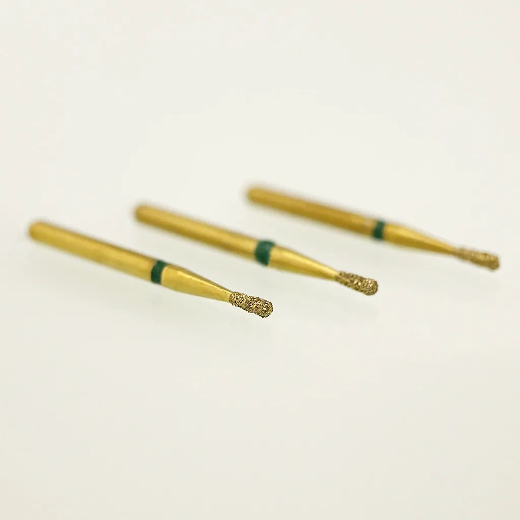 Three gold-colored dental burrs with green bands on a light beige background