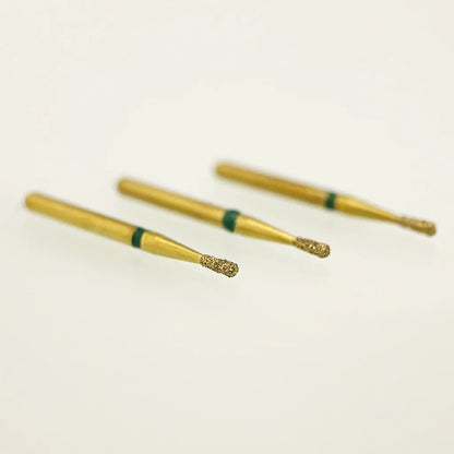 Three gold-colored dental burrs with green bands on a light beige background