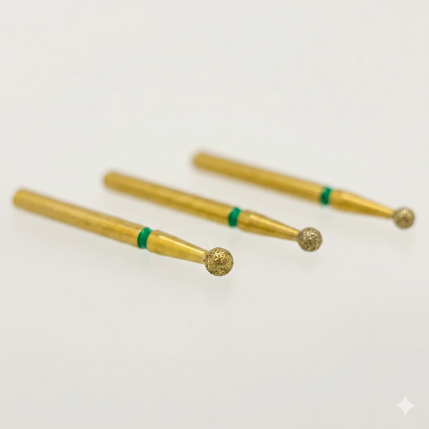 Three gold-colored dental burrs with green bands on a white background